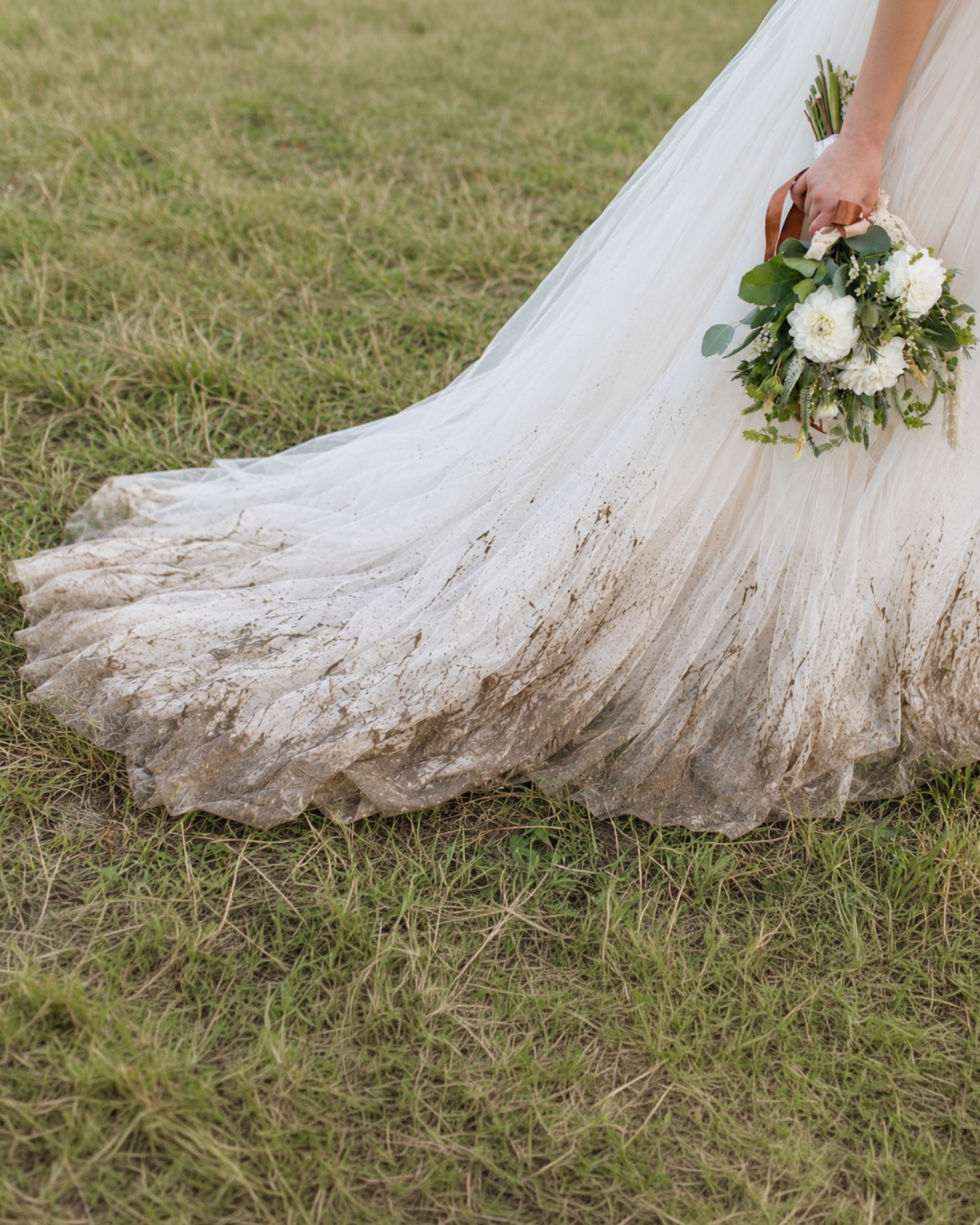 A wedding dress with visible dirt and staining beside a bouquet
